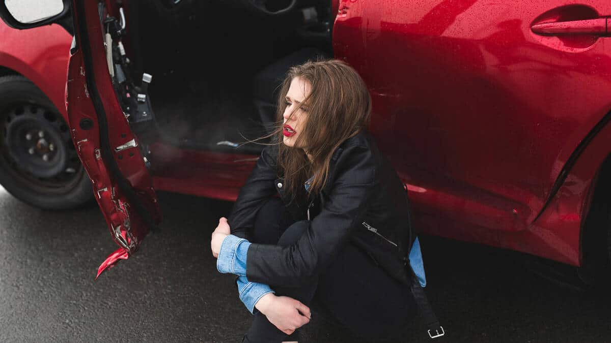 woman squatting near damage on her red car on driver's side