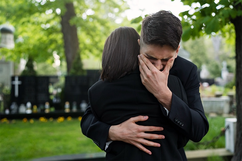 man weeping and embracing woman in graveyard