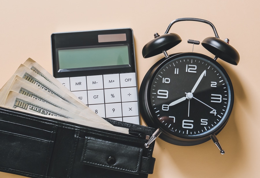 Imagen de una billetera con billetes de 100 dólares, una calculadora y un reloj.