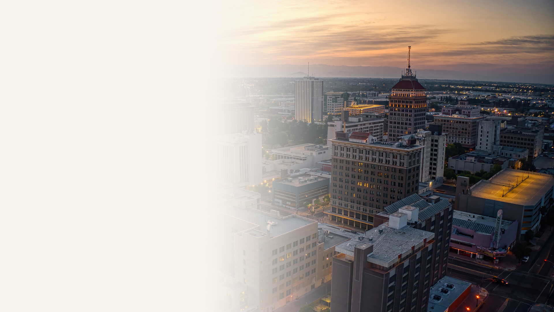 Downtown Fresno, California skyline at dusk with the Pacific Southwest Building's copper dome and distant mountains on the horizon