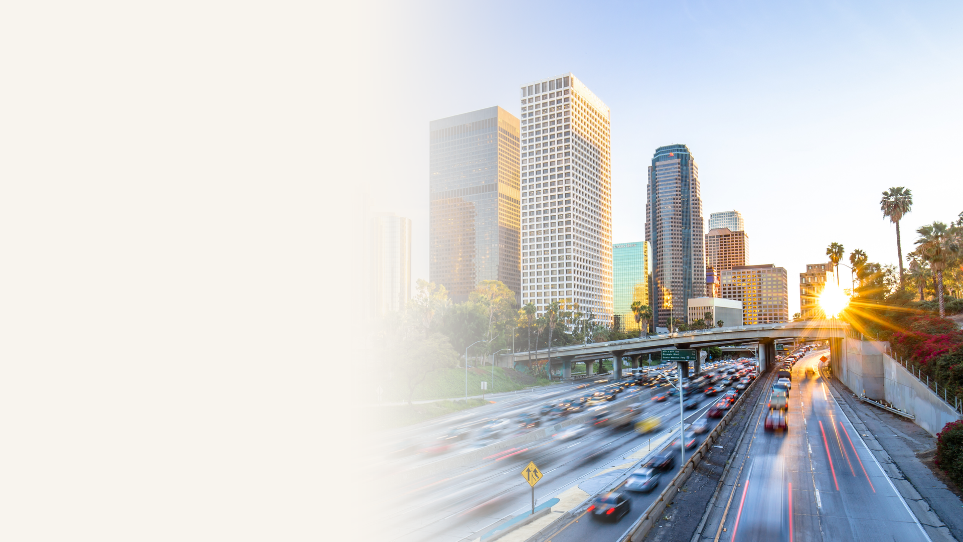 Downtown Los Angeles skyline at sunset with palm trees along the Harbor Freeway and rush-hour traffic motion trails