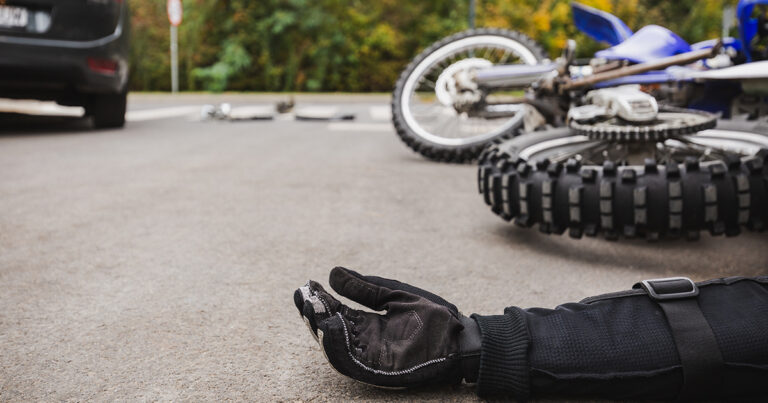 Man lying injured next to motorcycle after accident with car