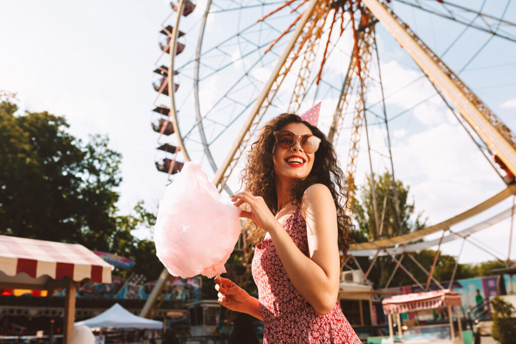 woman eating cotton candy in front of Ferris Wheel.